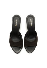 Mules de ante negro abiertos en la parte delantera con una amplia correa cruzada. Presentan una plantilla negra suave con "Mustang" grabado en dorado.