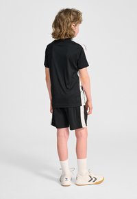 Czarna sportowa koszulka z krótkim rękawem z białymi akcentami po bokach, w połączeniu z czarnymi szortami. Białe sneakersy z czarnym paskiem i białe skarpetki.