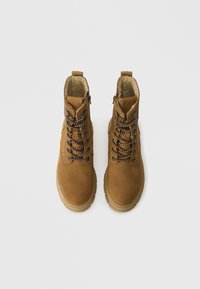 Bottes chelsea en cuir marron avec une surface texturée, featuring des lacets noirs et marron, des fermetures éclair sur le côté et une semelle épaisse beige. Accents de design tendance.