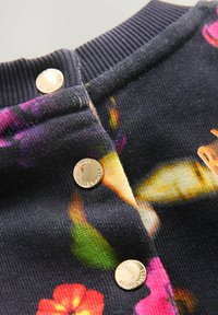 Tumeda taustaga lillemustriline kudumiskleit, millel on soonikkoes krae ja plaketil kolm kuldset metallist nööpi.