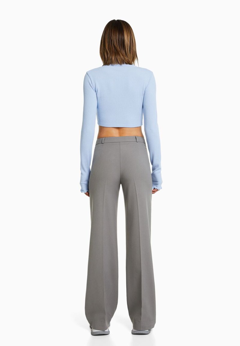 Top court côtelé bleu clair à manches longues associé à un pantalon large gris. Texture lisse, haut ajusté, pantalon taille haute avec poches.