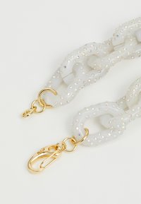 Balta ķēde, kas izgatavota no strukturēta materiāla ar mirdzošām rhinestone pūkām; iekļauj zelta aparatūru un omārs sprādzi. Gludas, noapaļotas saites.