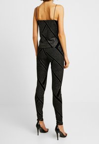 Svart glittrig topp med tunna remmar, kombinerad med matchande svarta leggings med diagonala silverränder och svarta högklackade skor.