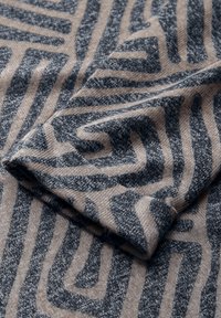 Dzianina z geometrycznym wzorem w ciemnoszarym i beżowym kolorze. Tekstura jest miękka, z podwiniętym brzegiem podkreślającym wzór.