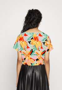 Top cropped de mangas curtas em um padrão floral colorido, com flores laranja e amarelas sobre um fundo verde menta. Combinado com uma saia plissada preta.