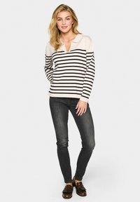 Lange mouwen, geknoopte poloshirt in crème met zwarte horizontale strepen. Gecombineerd met donkere skinny jeans en bruin loafer.
