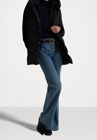 Černý péřový kabát, modré zvonové džíny s vysokým pasem a zapínáním na knoflíky, kotníkové boty a černý rolák. Hladké textury.