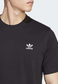 Juodas medvilninis marškinėlis su apvalia apykakle, su mažu baltu siuvinėtu Adidas logotipu kairėje krūtinės pusėje. Lygi tekstūra, trumpomis rankovėmis.