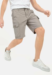 Graue Cargo-Shorts mit Seitentaschen, leicht über knie-langer Schnitt, kombiniert mit weißen Sneakers mit grauen Akzenten. Lässiger Schnitt und Design.
