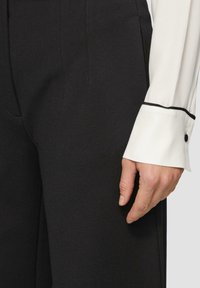 Zwarte broeken met een zachte textuur, met een op maat gemaakte pasvorm en een subtiele plooi. Het witte shirt heeft een contrasterende zwarte manchetrand.