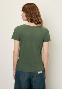 T-shirt in cotone verde con scollatura rotonda, maniche corte e design semplice e senza cuciture. Indossato con pantaloni corti in denim blu larghi.