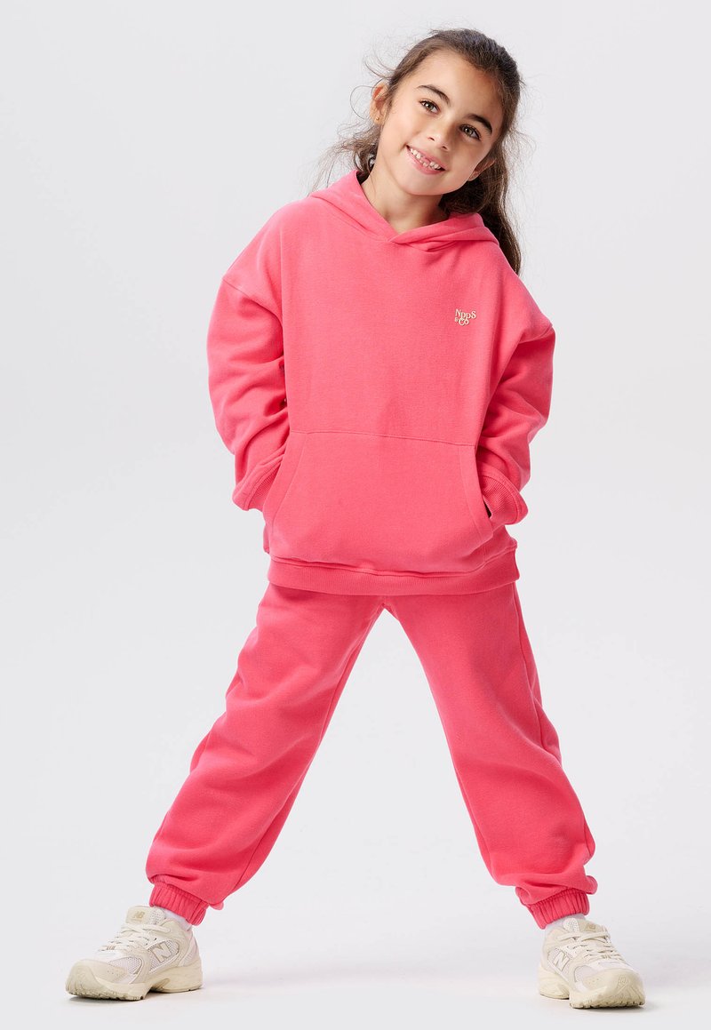 Roze hoodie en bijpassende joggingbroek van zachte stof, met een voorzak en geribde boorden, gecombineerd met witte sportieve sneakers.