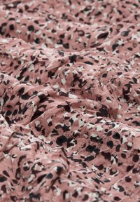 Rosa gemusterter Stoff mit schwarz-weißen Flecken, der eine strukturierte, knittrige Erscheinung aufweist. Geeignet für Bekleidung oder Wohnkultur.