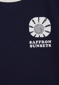 Tmavomodré tričko s krátkym rukávom, na ktorom je biely slnečný motív so špirálovitými detailmi a nápis „SAFFRON SUNSETS" pod ním.