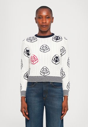 Pull en tricot blanc avec un motif en câble, des designs de roses bleues et un accent en rose rouge. Col ras du cou côtelé bleu marine et poignets. Coupe cropped.