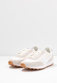 Beiga sneakers med ovandel i mocka och tyg, vit Nike-swoosh, krämfärgade snören och en strukturerad orange gummisula.