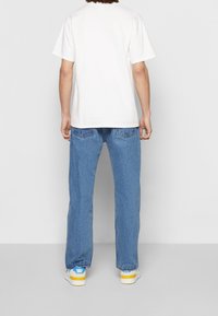 Vit bomullströja med avslappnad passform, kombinerad med blå denimjeans. Skorna har vit bas med gula och blå detaljer. Avslappnad stil.