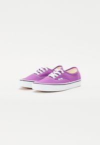 Purple canvas shoes with white laces and black accents, featuring a rounded toe and flat white rubber sole. Classic low-top design.