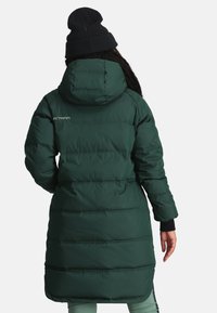 Groene pufferjas met een capuchon, geribbelde manchetten en een middellange snit. Heeft horizontale stiksels en een logo op de bovenste linkerzijde.
