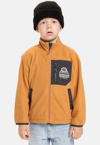 Fleeceová bunda v oranžové barvě s černými akcenty. Obsahuje zipovou náprsní kapsu, boční kapsy a vysoký límec. Nositelná s černou pletenou čepicí.