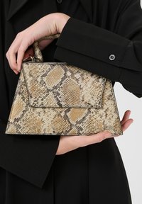 Borsa strutturata in materiale beige chiaro e marrone con motivo a serpente, dotata di manico superiore e chiusura a patta, con un sottile marchio sul lato.