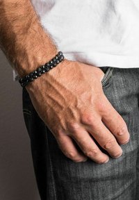 Black bead bracelet featuring spherical and textured lava rock beads, accentuated by polished black beads, worn on a wrist with visible veins.