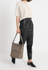 Grå läder toteväska med en framficka, silverfästen och en lång axelrem. I kombination med en beige topp och svarta läderbyxor.