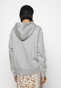 Felpa grigia realizzata in tessuto morbido, con un ampio cappuccio, spalle scese e orlo a coste. Vista posteriore mostrata con dettagli di design minimali.