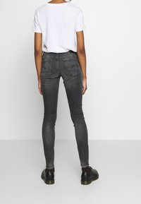 Černé džíny s přiléhavým střihem a vybledlým efektem, pětikapsový design a viditelné švy. Kombinovány s jednoduchým bílým tričkem a černými botami.