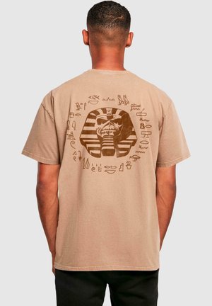 Beige t-shirt met korte mouwen met een grafisch ontwerp van een farao omgeven door hiërogliefen, gedrukt in bruin op de achterkant.