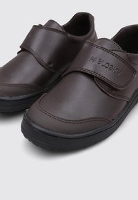 Zapatos sintéticos marrones con un acabado suave, que presentan una correa de Velcro y suela de goma. Costuras reforzadas en los bordes y logotipo "PABLOSKY".
