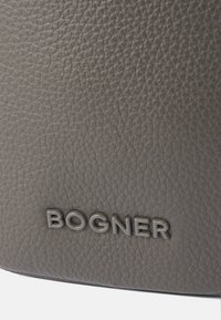 Šedá texturovaná kožená taška má na přední straně embosované logo "BOGNER", které vystihuje jemnou zrnitou strukturu a hladký povrch.