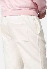 Weiße Sweathosen aus strukturiertem Stoff mit zwei Gesäßtaschen, kombiniert mit einem rosa Sweatshirt. Sichtbarer elastischer Bund.