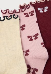 Três pares de meias: amarelas com nervuras e uma borda escura, cor-de-rosa com nervuras e laços castanhos, e bordeaux com nervuras. Cada par apresenta um topo com babados.