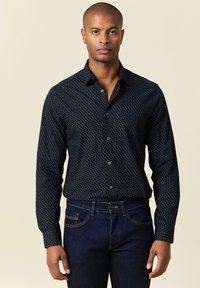 Camisa de botones azul marino con un pequeño patrón de lunares blancos, de manga larga y con cuello, combinada con jeans azul oscuro.