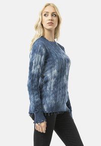 Pull en maille bleu avec un col rond, une bordure effilochée et un motif texturé. Le matériau semble doux avec un léger éclat.
