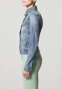 Ljust blå denimjacka med två bröstfickor, knäppning fram och en figursydd passform. Strukturerad tyg med ett lätt slitet utseende.