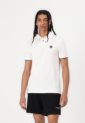 White polo shirt with a black logo on the chest, short sleeves, and a black trim on the collar; worn with black shorts featuring yellow text.