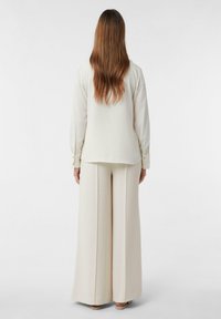 Kremowa, długorękawowa bluzka z zapięciem na guziki przy mankietach, w połączeniu z szerokimi spodniami o wysokim stanie, obie z gładkiego materiału.