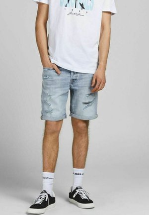 Světle modré denimové šortky s opotřebenými detaily a ohrnutými lemy, spárované s bílým tričkem s potiskem a černými teniskami, doplněné bílými ponožkami.