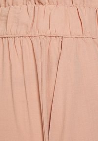 Detailní záběr na světle růžovou shromážděnou látku s viditelným stehem a záhyby, který ukazuje texturu a detaily materiálu.