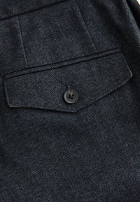 Tissu en denim foncé avec une poche plaquée ornée d'un motif cousu et un bouton noir à quatre trous.