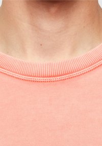 Light pink crew neck t-shirt featuring a ribbed collar and smooth texture, with visible stitching details on the neckline.