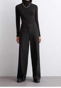 Schwarzer Rollkragenpullover mit langen Ärmeln, kombiniert mit hoch geschnittenen, weit geschnittenen Nadelstreifenhosen. Bietet eine figurbetonte Silhouette und eine glänzende Halskette.