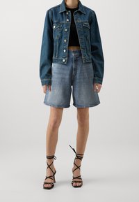 Jeansjacka i mörkblått med silverknappar, tillsammans med ljusblå denim shorts. Svarta remsandaler fulländar outfiten.