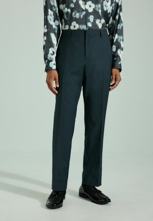 Pantalons taillés en vert foncé avec une coupe droite, présentant des plis à l'avant. Associé à une chemise à manches longues noire et blanche à fleurs à motifs et des chaussures noires.