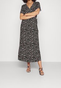 Robe portefeuille noire à motifs floraux avec des manches courtes, dotée d'un décolleté en V, de feuilles vertes et de fleurs roses, atteignant la longueur mi-mollet. Sandales à lanières portées.