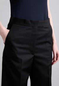 Svarta skräddarsydda byxor med en slät textur, som har sidofickor och en rak front. Bärs med en marinblå topp som framhäver midjebandet.