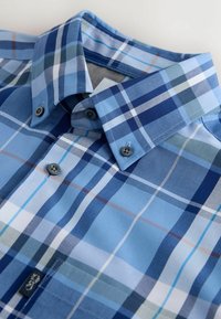 Chemise à carreaux bleue et blanche avec col boutonné et boutons noirs sur le devant plié.