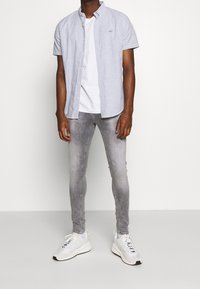 Košile s krátkým rukávem, pruhovaná v modré a bílé barvě, přes bílém tričku, v kombinaci se světle šedými slim kalhotami a bílými teniskami.